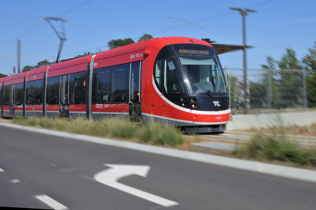 modern red light rail vehicle travelling along tracks in Canberra on a sunny day