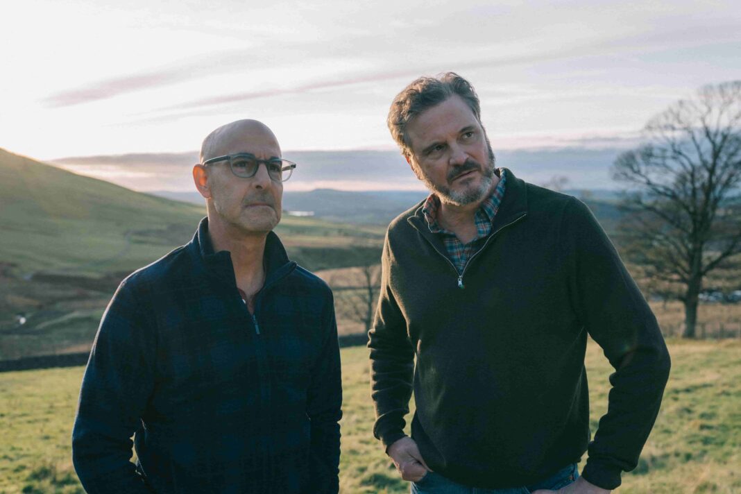 Two mature male actors, Stanley Tucci and Colin Firth, standing in the English countryside