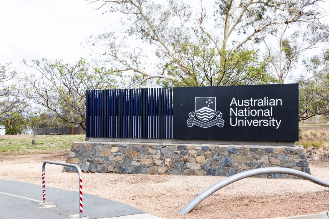 Big black sign with Australian National University in white text on a stonework foundation near cycle path