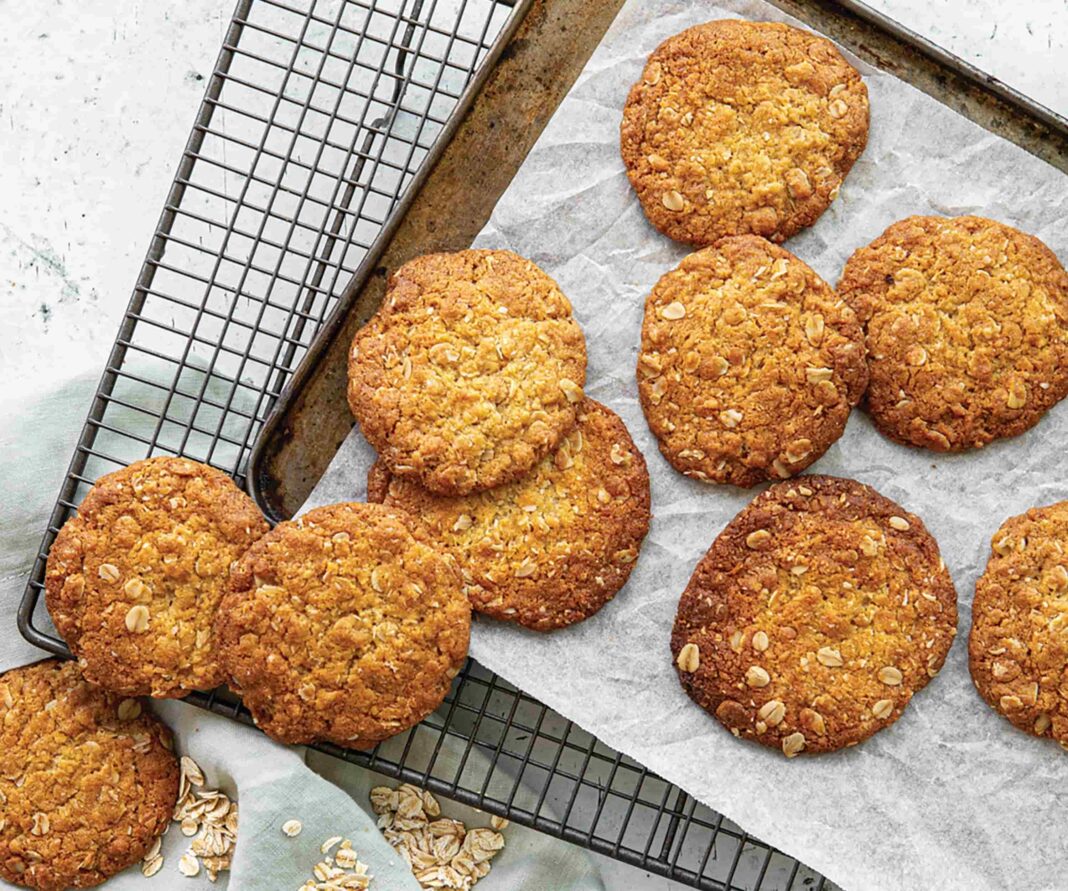 10 golden Anzac biscuits scattered on a baking tray