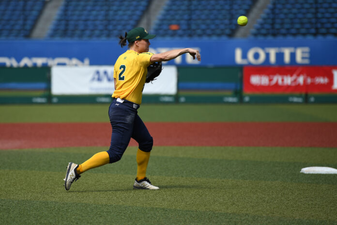 ACT Olympic hopeful Clare Warwick wears a green and gold uniform and is pictured in action, throwing a softball.