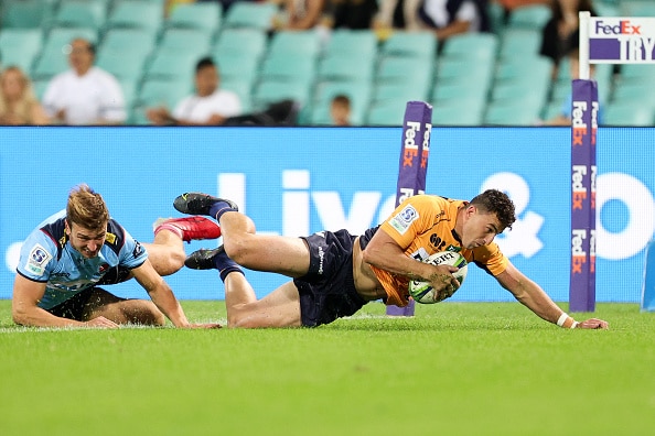 rugby player in gold jersey and dark blue shorts stretching across the try line to score a try with opposition player at his heels