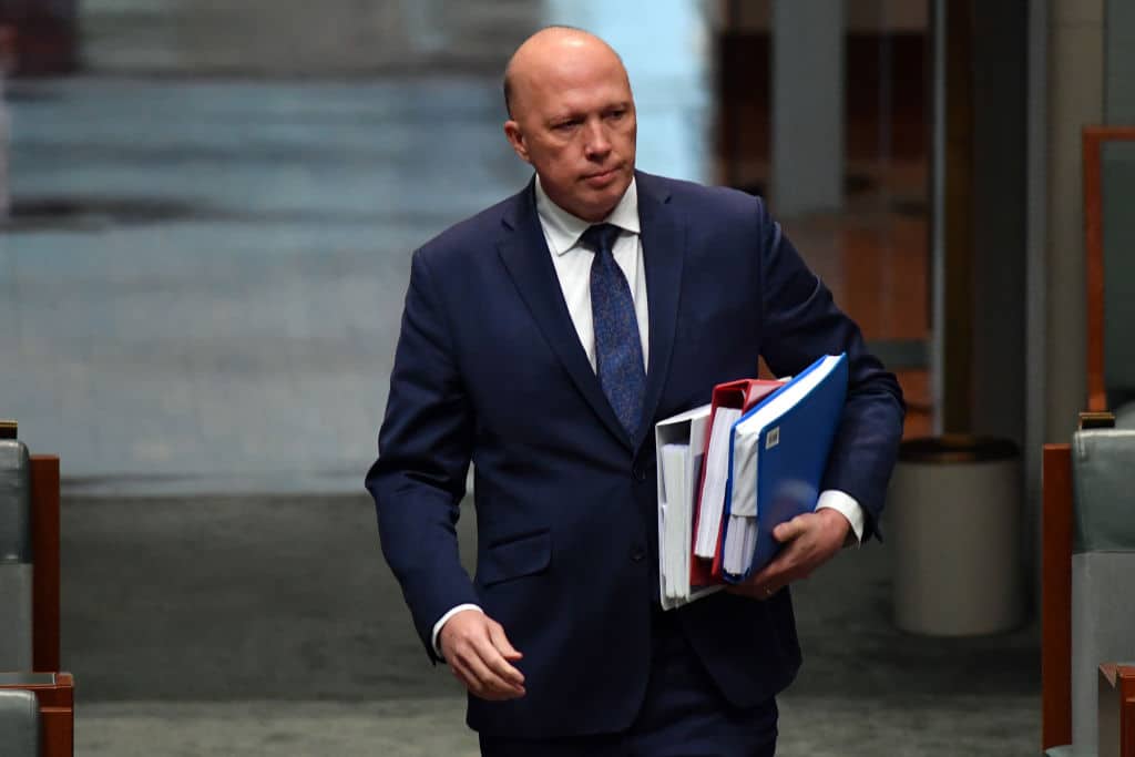 Australian Defence Minister Peter Dutton, a bald middle-aged man in dark blue suit with white shirt and blue tie, holding three ring binder folders while walking