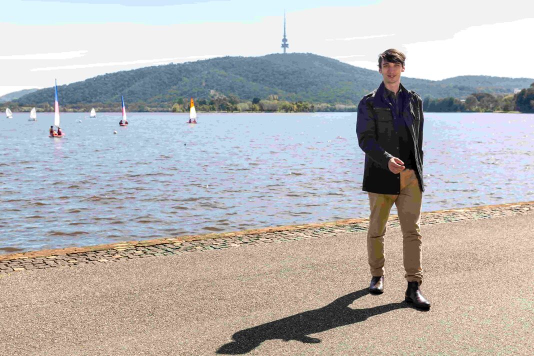 Well-dressed young man walking beside Lake Burley Griffin in Canberra with Black Mountain tower in background and sailboats on the water