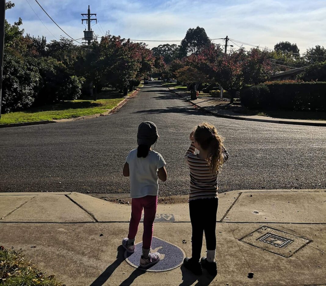 Two children on a footpath taking a photo of their leafy Canberra suburb