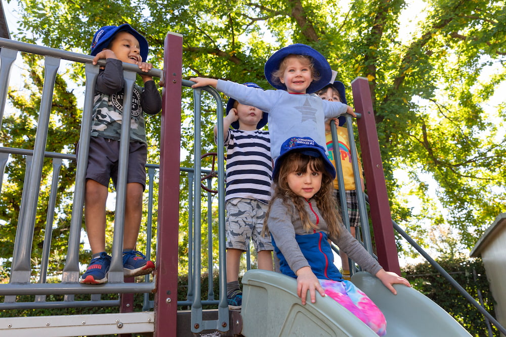 A group of preschool children climb over play equipment