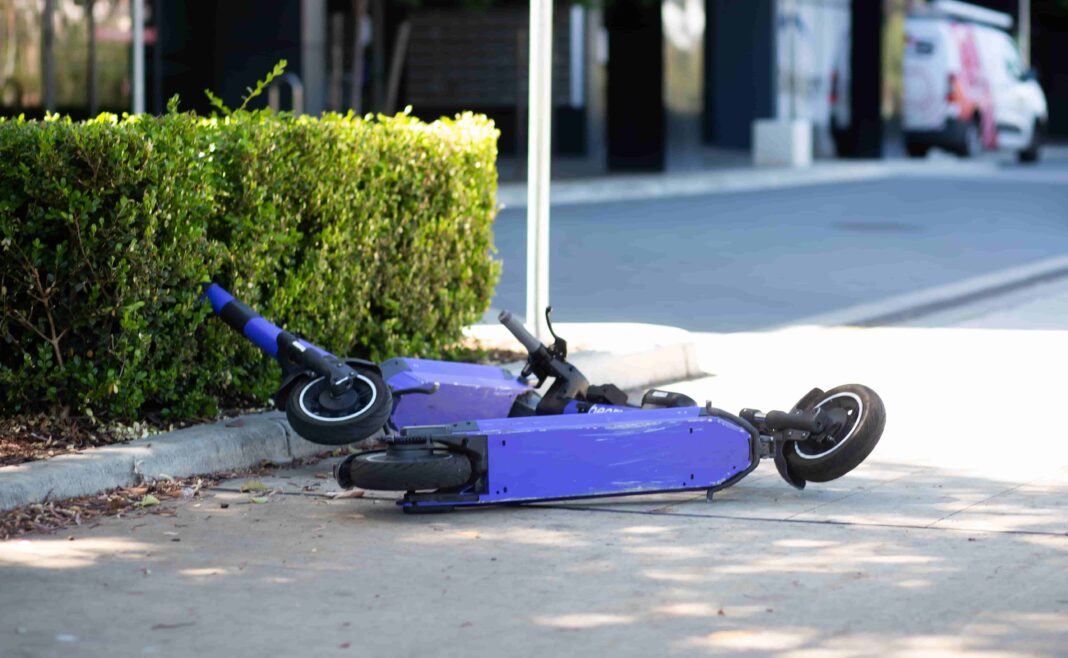 Two purple e-scooters lie on their side on a footpath