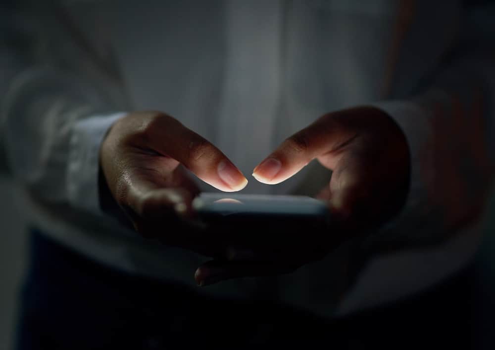 A pair of hands holding a smart phone are partially lit up by the screen, searching for sexual assault support services.