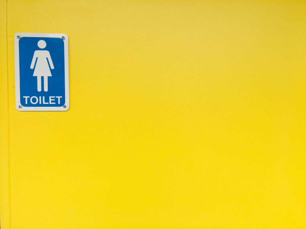 blue and white female toilet sign on bright yellow wall