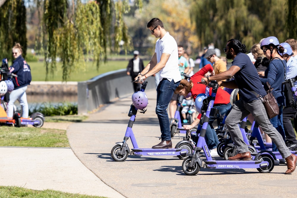 group of people riding purple e-scooters in a park