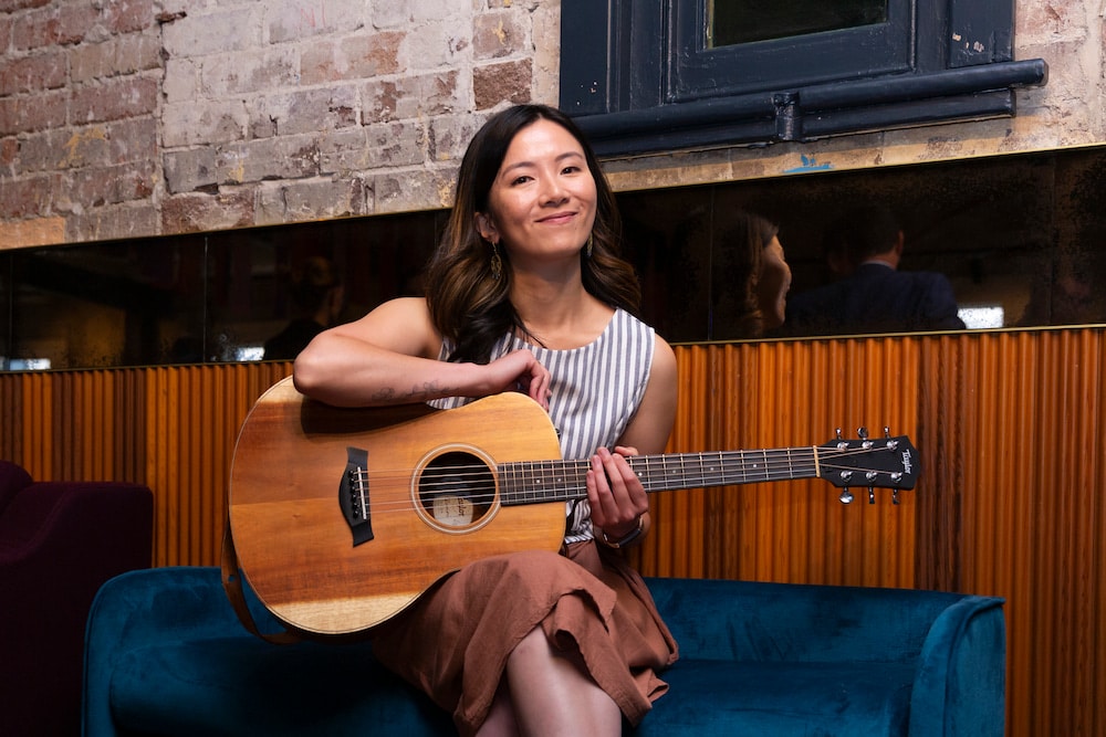 Young smiling Korean woman sitting and holding acoustic guitar