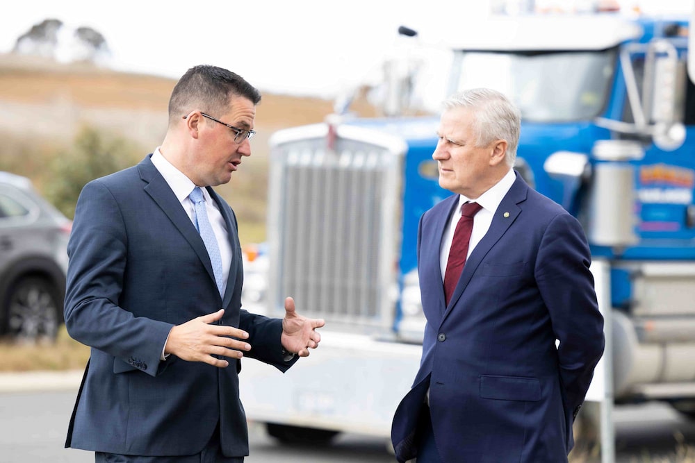 Two male politicians in business suits speaking in front of big blue truck parked by the roadside