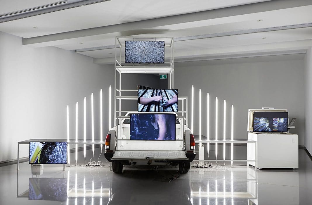 a video art installation comprising a white ute and five TV screens in a white gallery space