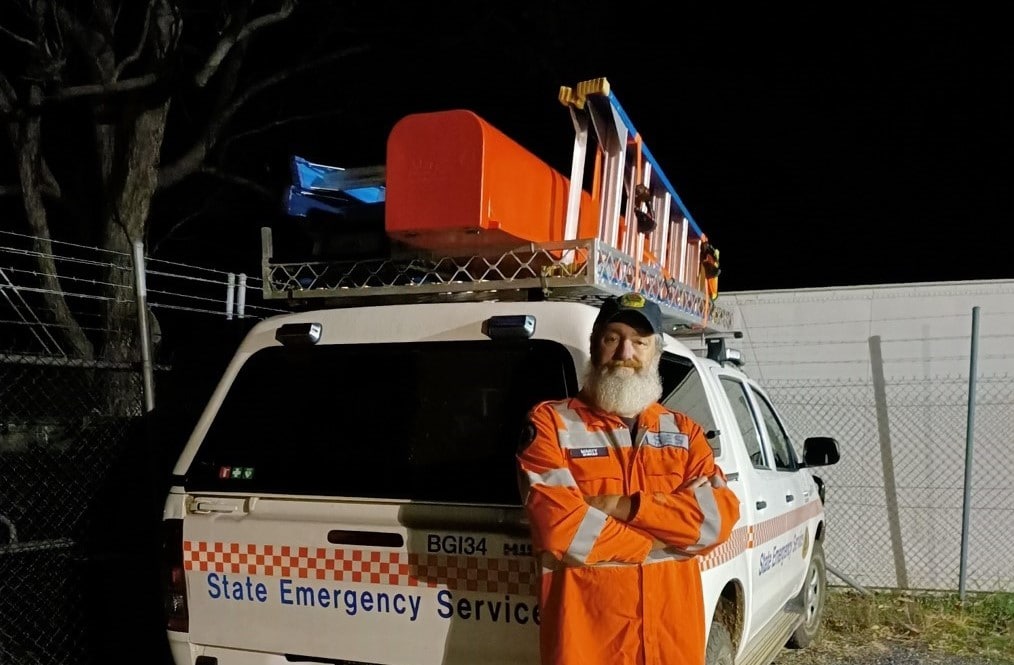 Older bearded male in orange hi-viz overalls standing near a NSW State Emergency Service van