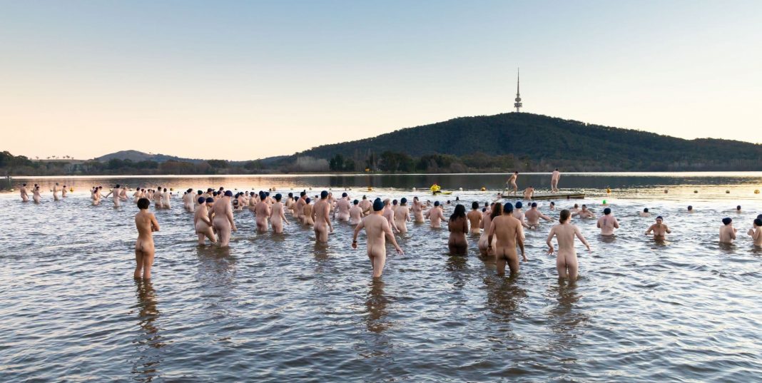 hundreds of naked adults wading into Lake Burley Griffin on a winter morning at sunrise