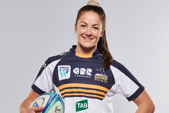 smiling young woman in Brumbies rugby jersey and holding a rugby ball