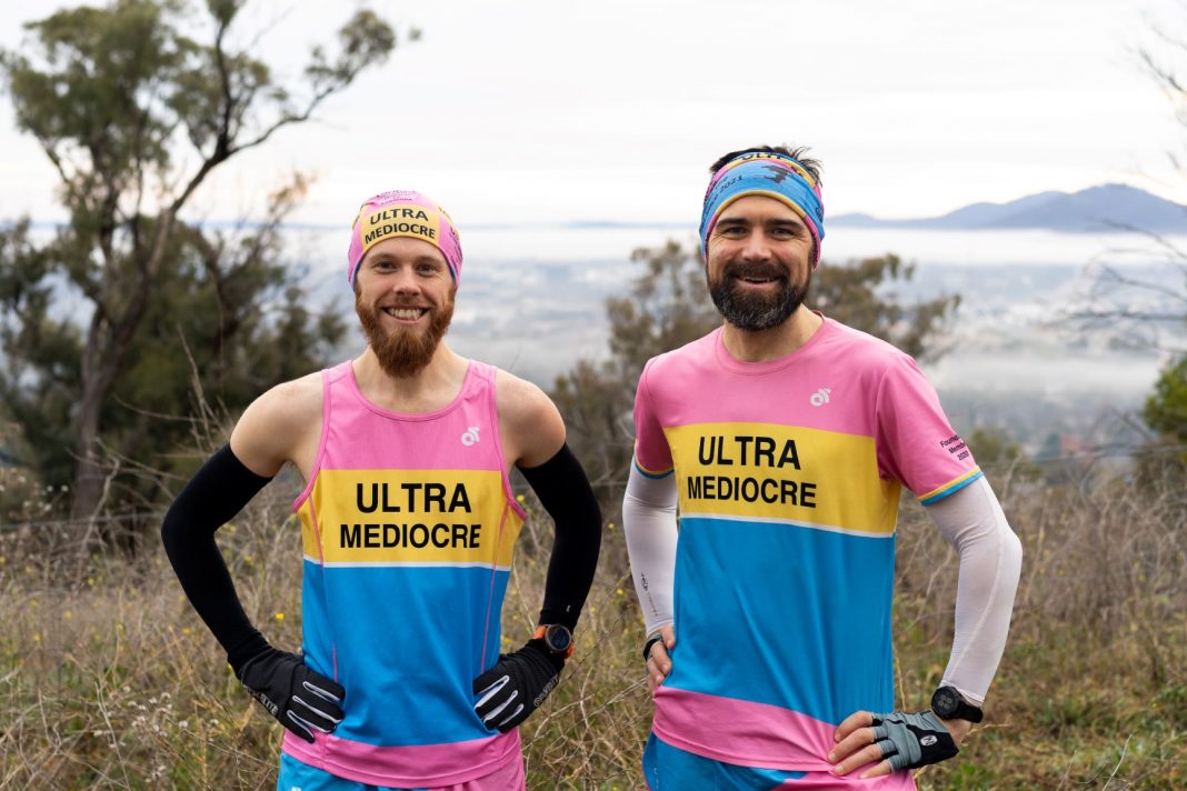 Two men in colourful running singlets and beanies with views of fog over Canberra in the background
