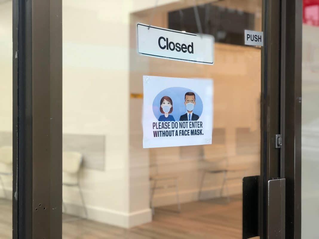 Closed sign on door to business with a second sign requesting masks be worn inside