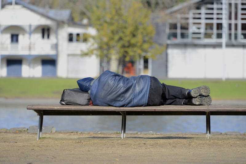 homeless man sleeping on a park bench in a nice suburb