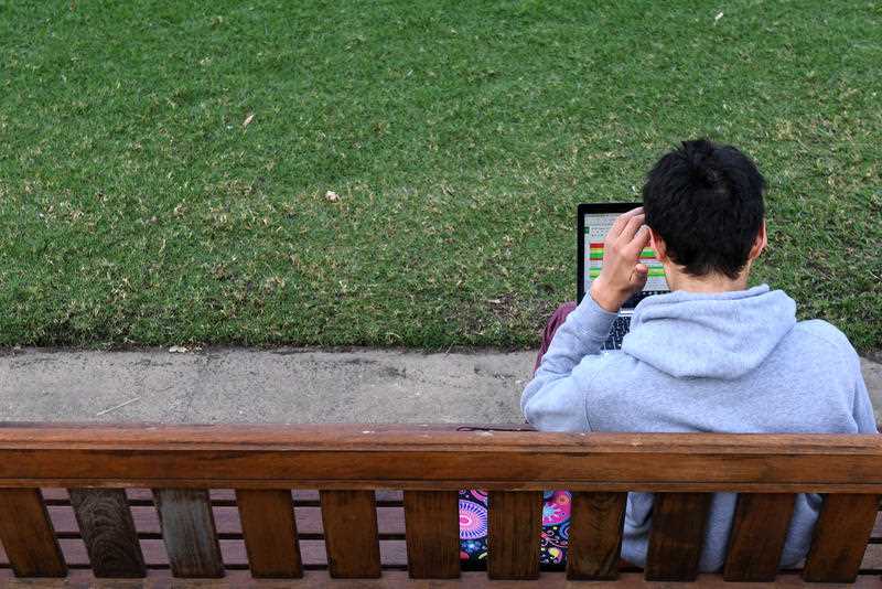 A male student works on a laptop outdoors on a university campus