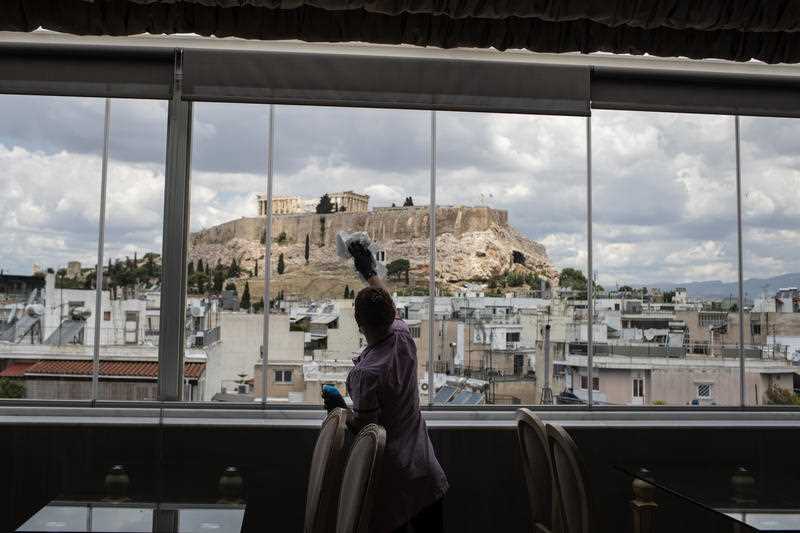 woman cleaning windows inside restaurant with views to the Acropolis in Athens