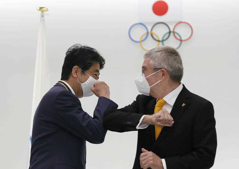 Former Japanese Prime Minister Shinzo Abe and Thomas Bach, President of the International Olympic Committee bump elbows while wearing masks