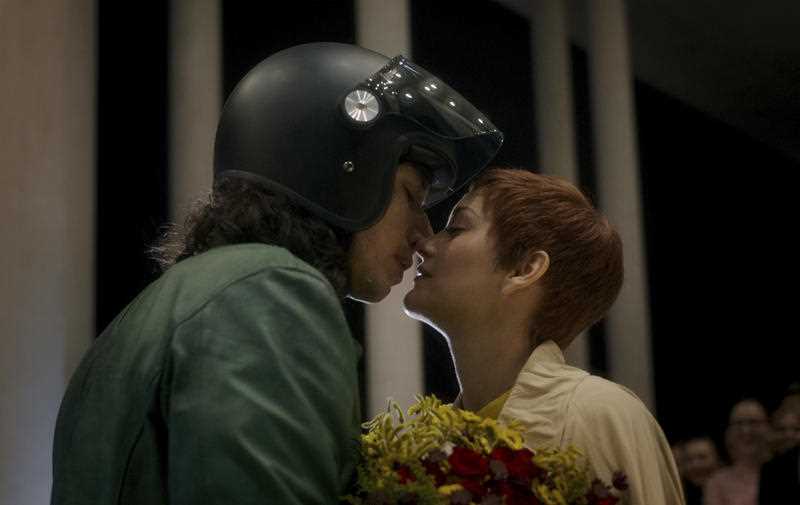 tall dark haired male actor in motorcycle helmet kissing woman with short red hair