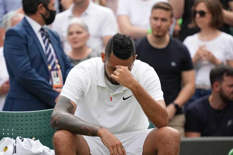downcast tennis player Nick Kyrgios sitting courtside with his head in his hands
