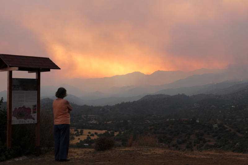 Woman in Cyprus looking at bushfire blazing in distant hills