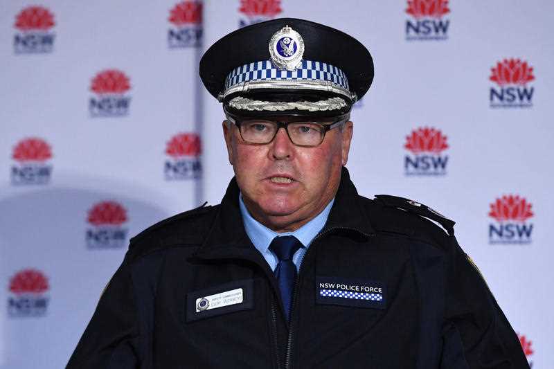 middle aged male police commissioner in full uniform, cap and glasses speaking at press conference