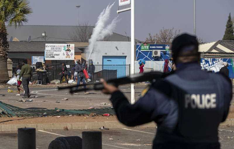 South African police officer holding firearm as people protest or loot in the streets