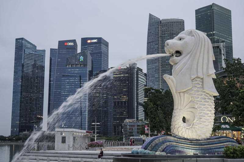 A woman is dwarfed by the Merlion statue and buildings of the financial district in Singapore