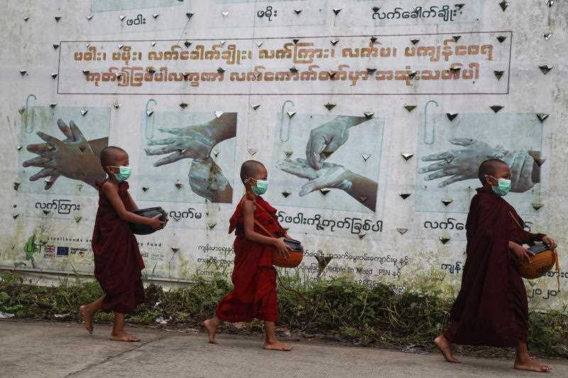 Buddhist novice monks wearing face mask walk past the COVID-19 awareness signboard as they collect morning alms in Yangon, Myanmar.