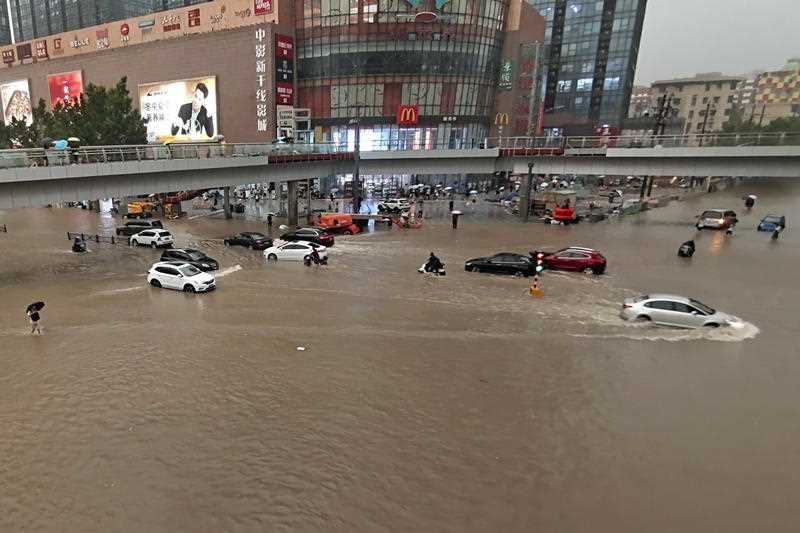 People and vehicles moving through flooded streets of city in China