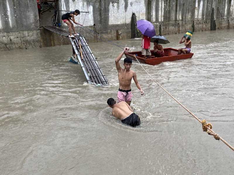 Filipinos cross a damaged bridge along a swelling river in Bacoor town