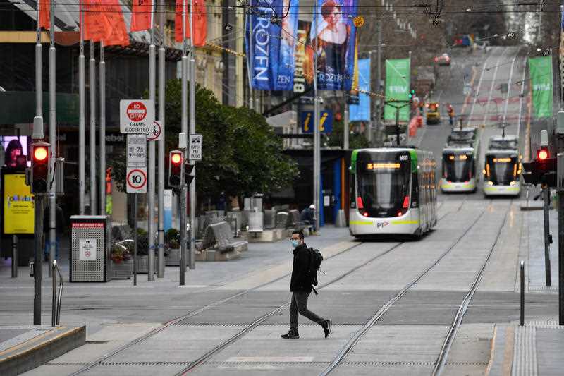 A person wearing a face mask crosses a street in Melbourne during lockdown