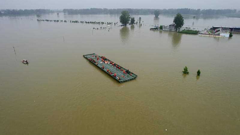 Rescuers ride a motorized raft bridge to evacuate residents from a flooded rural area in Xinxiang in central China's Henan Province