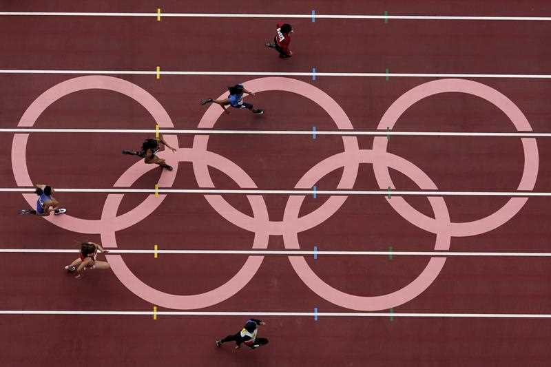 overhead view of runners sprinting past some Olympic rings during the first round of the women's 100-meter at the 2020 Summer Olympics