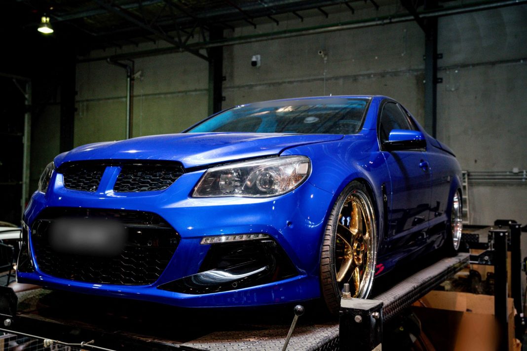 a hotted up bright metallic blue Holden ute on a trailer in a garage