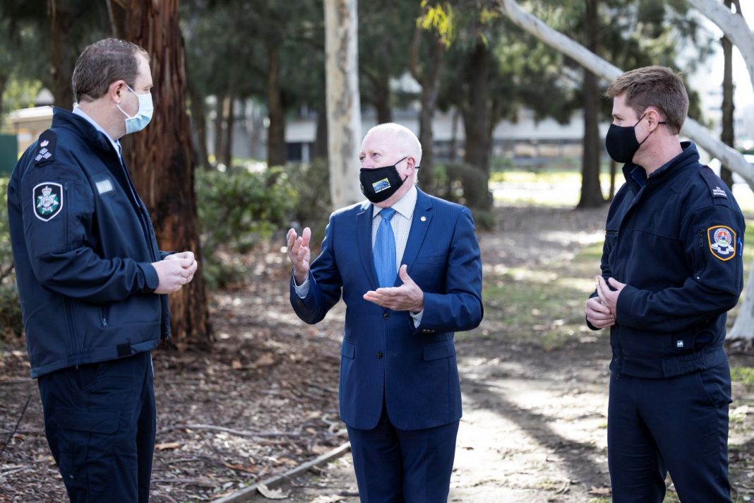Two men in uniform flanking man in business suit all wearing face masks