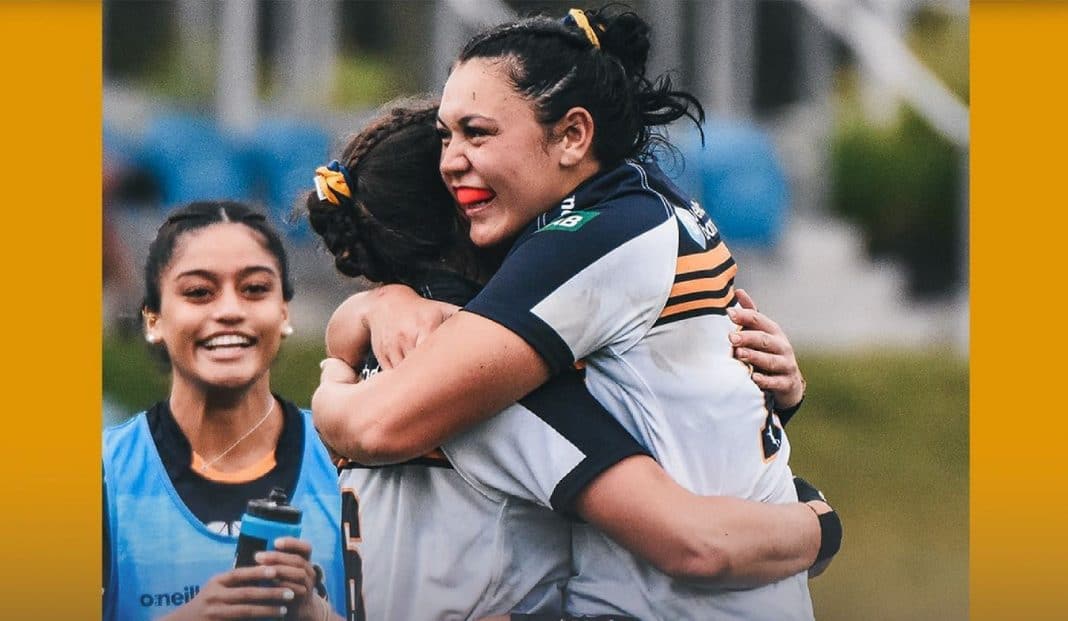 Two female rugby players celebrating victory with a hug as a teammate looks on smiling