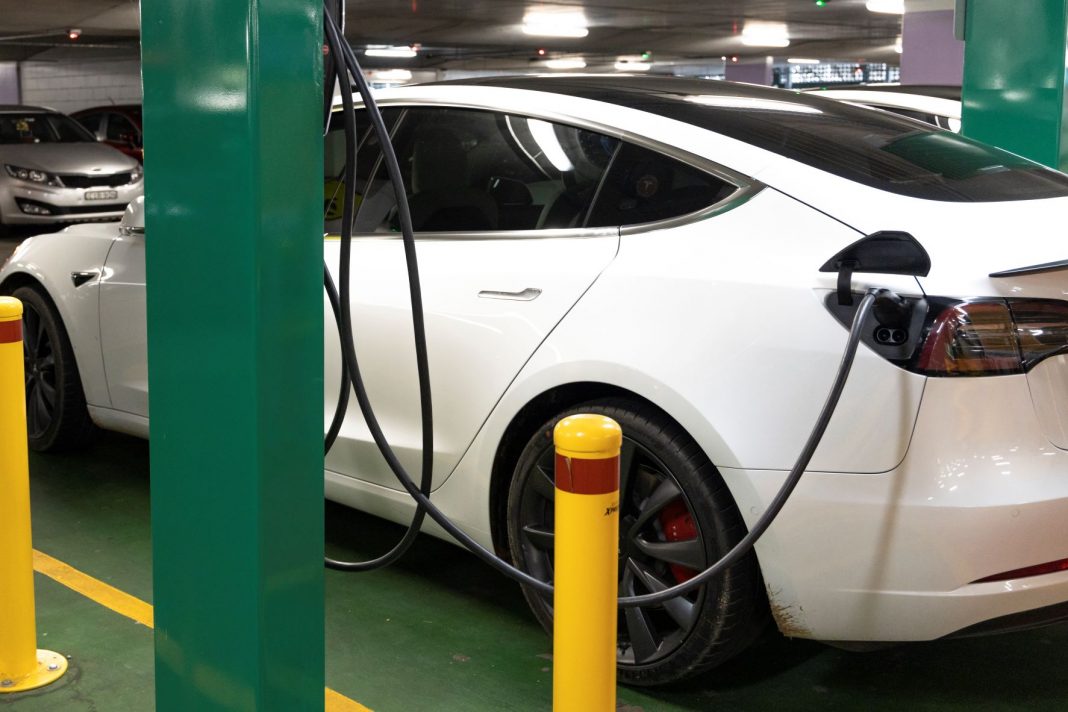 A white Tesla electric car plugged into a recharging station