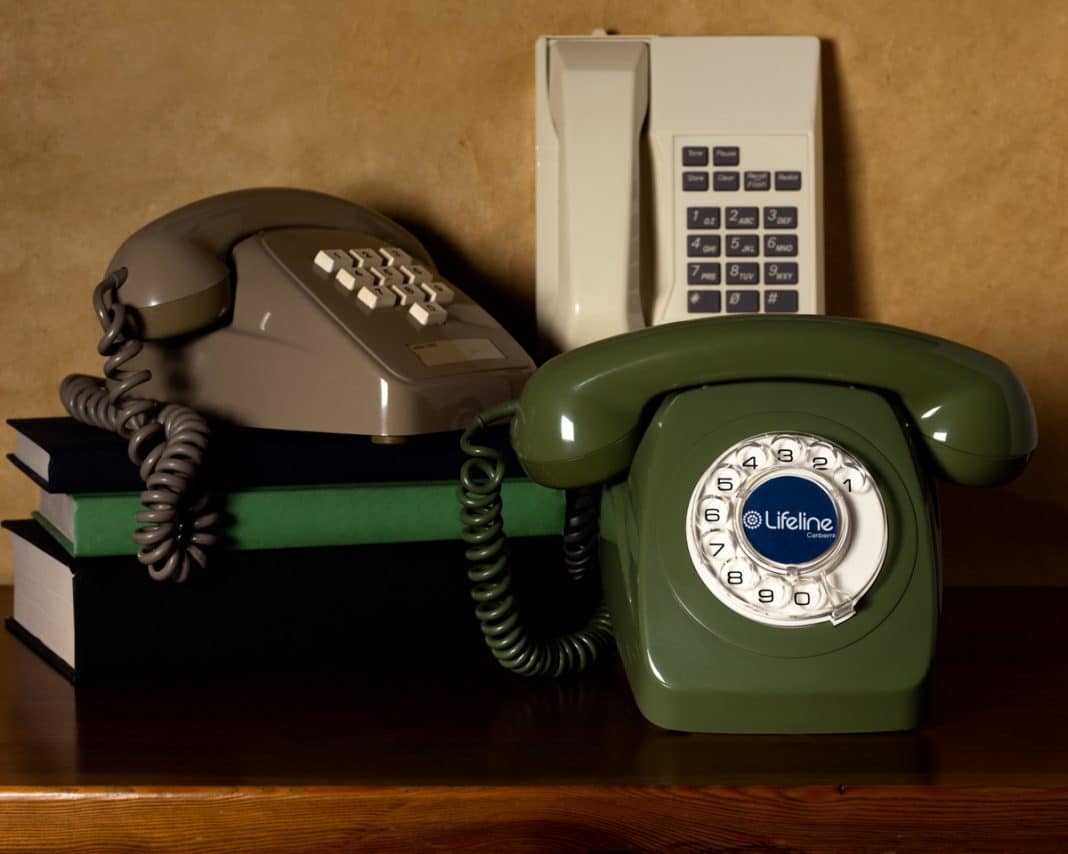 A collection of 3 old-style phones, the front one with a Lifeline Canberra 13 11 14 sticker on the dial