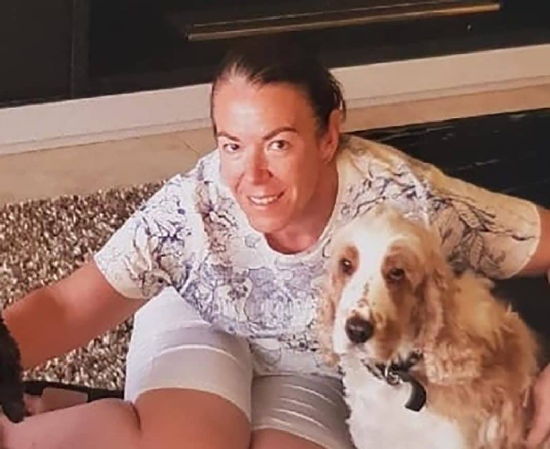 middle aged woman in shorts ant t-shirt sitting on the floor with her tan and white dog