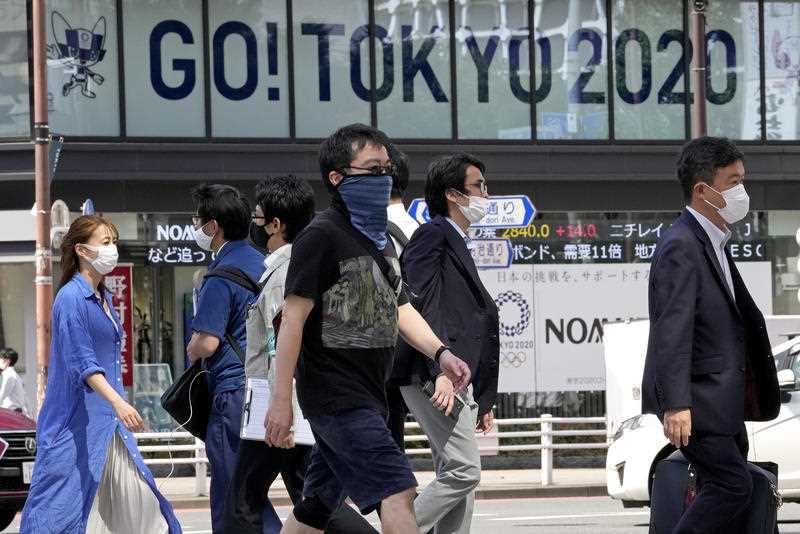 people wearing masks in streets of Toyko overshadowed by 'Go! tokyo 2020' Olympics sign