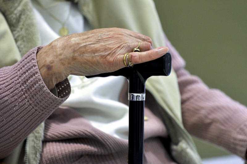 An elderly woman uses a walking stick to aid her mobility