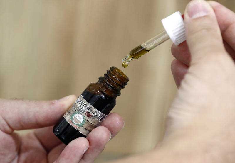 Hands holding a vial and a dropper of medical cannabis oil