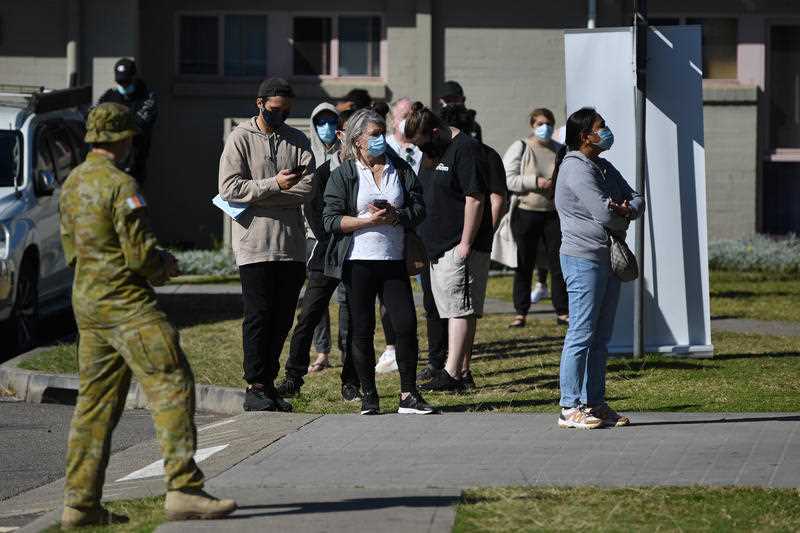 An Australian soldier in camouflage watches as members of the public wait in line at a vaccination clinic at Wattle Grove in Sydney