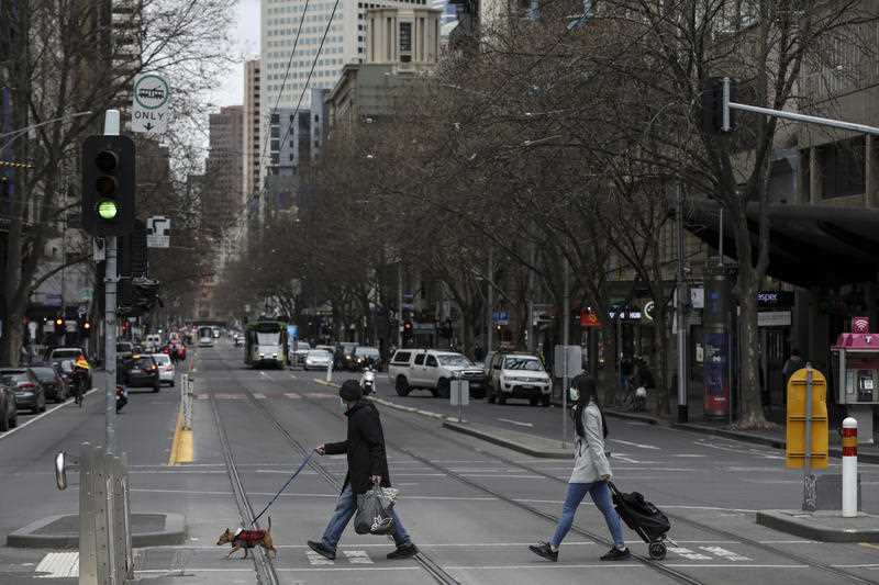 Two pedestrians wear face masks as they cross a quiet road in the Melbourne CBD