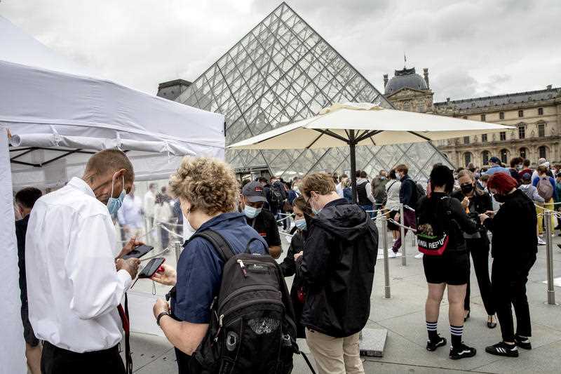 Visitors show their pass to enter the Louvre museum in Paris, Friday, Aug. 6, 2021